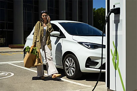 femme avec un sac de course à la main en train de recharger une voiture hybride
